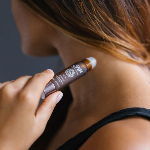 A woman applying pain release roll-on to their neck